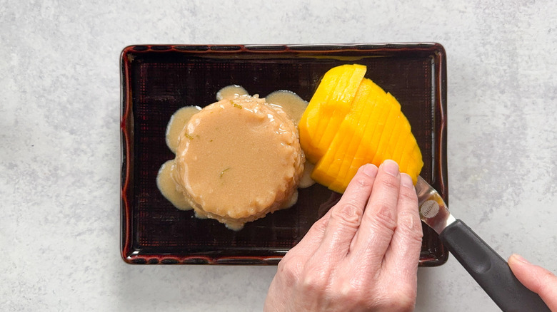 Adding sliced mango to sticky rice and coconut sauce on plate