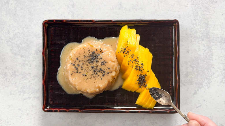 Sprinkling black sesame seeds over mango sticky rice on plate