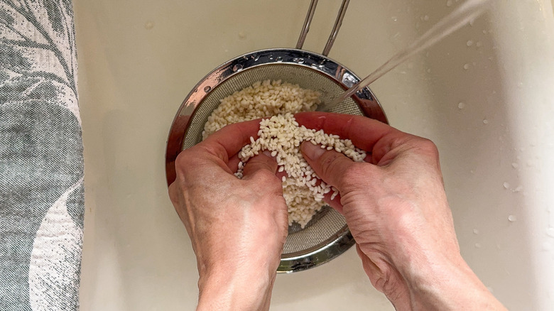 Washing and massaging sweet rice grains in a mesh sieve in sink