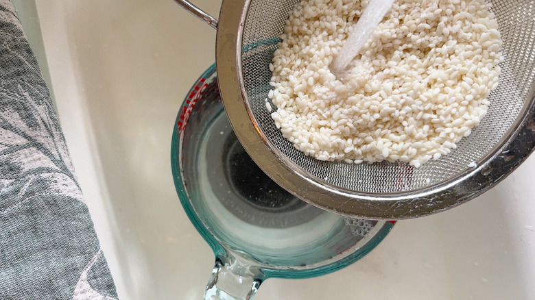 Rinsing sweet rice kernels in fine mesh sieve over glass measuring up in sink