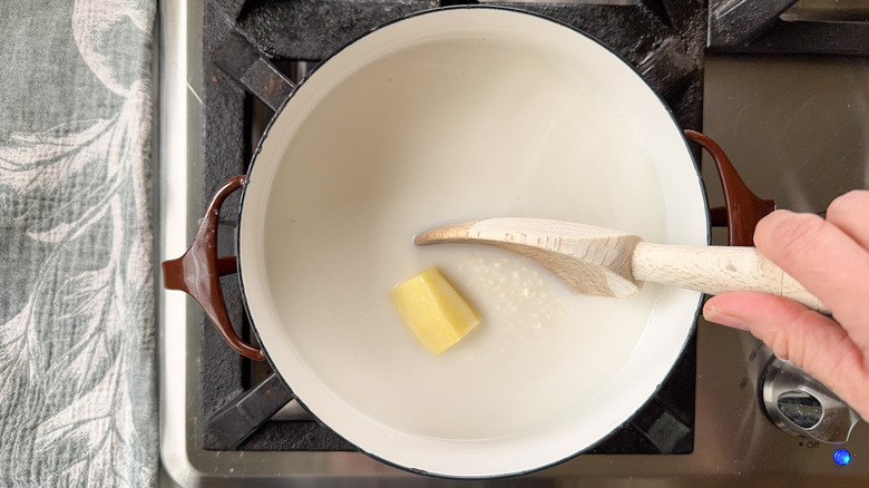 Stirring sweet rice, coconut milk, and ginger root with wooden spoon in saucepan