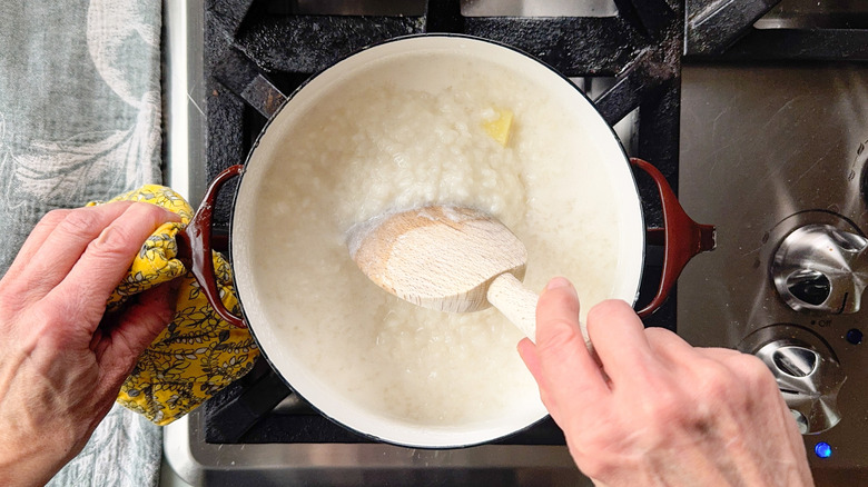 Stirring sticky rice with wooden spoon in pot on stovetop