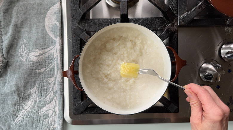 Removing a piece of peeled ginger root from sticky rice in pot on stovetop