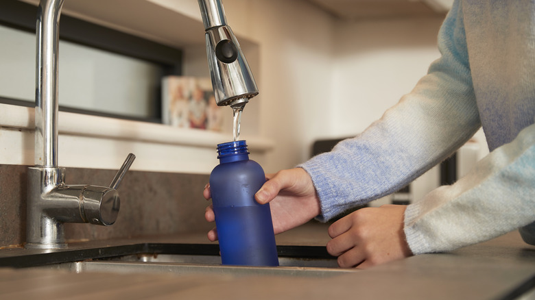 Person refilling reusable water bottle in sink