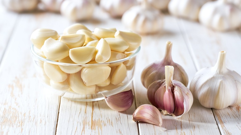 A glass bowl full of peeled garlic beside whole garlic cloves.