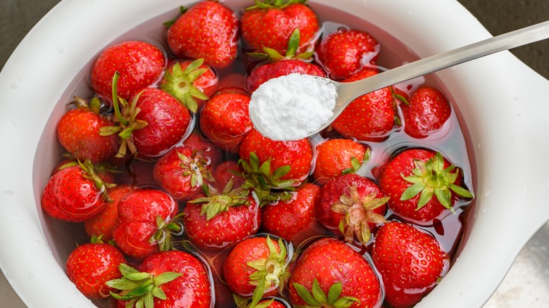 baking soda being added to a bowl of strawberries and water