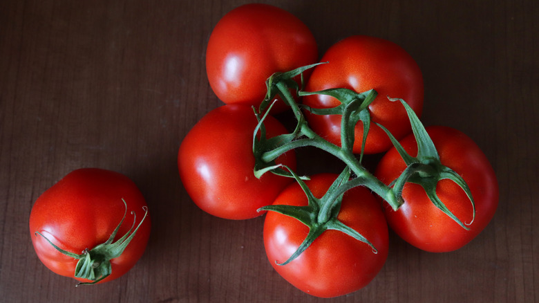 Tomatoes with vine sitting on a wood surface