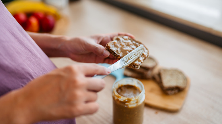 A woman spreading peanut butter on a piece of toast