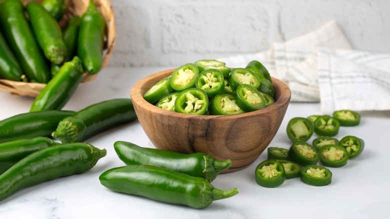 a bowl of sliced jalapeños surrounded by whole peppers