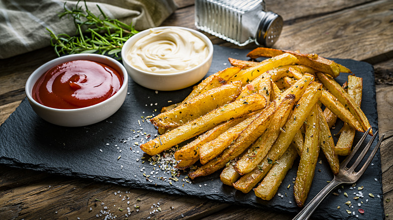 homemade seasoned fries on a wooden board with bowls of ketchup and mayo