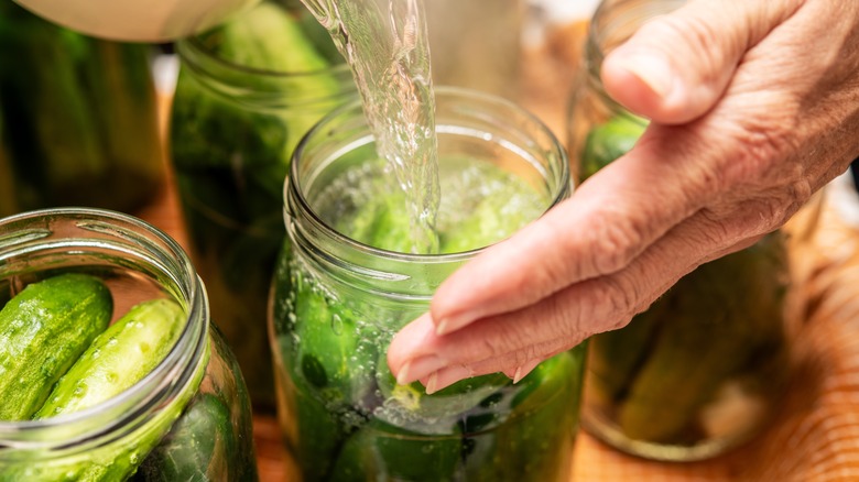 Person pouring brine into jar of cucumbers