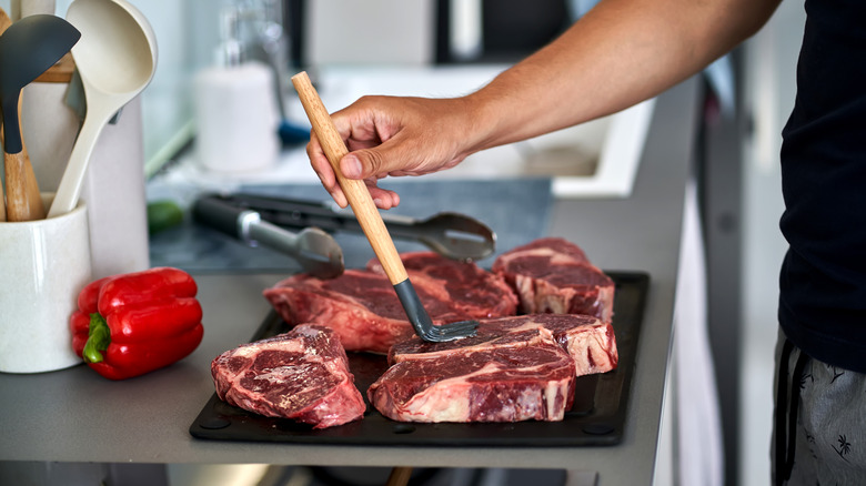 A hand brushing marinade onto a tray of steaks.