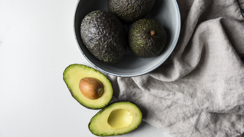 avocados in a bowl next to avocado halves