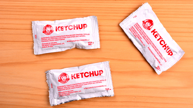 Three Wendy's ketchup packets on wood table