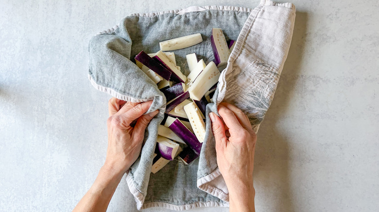 Patting sliced Chinese eggplant dry with kitchen towel