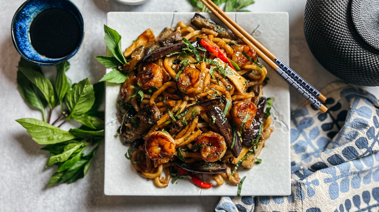 Shrimp and eggplant stir-fry on plate with chopsticks and garnish