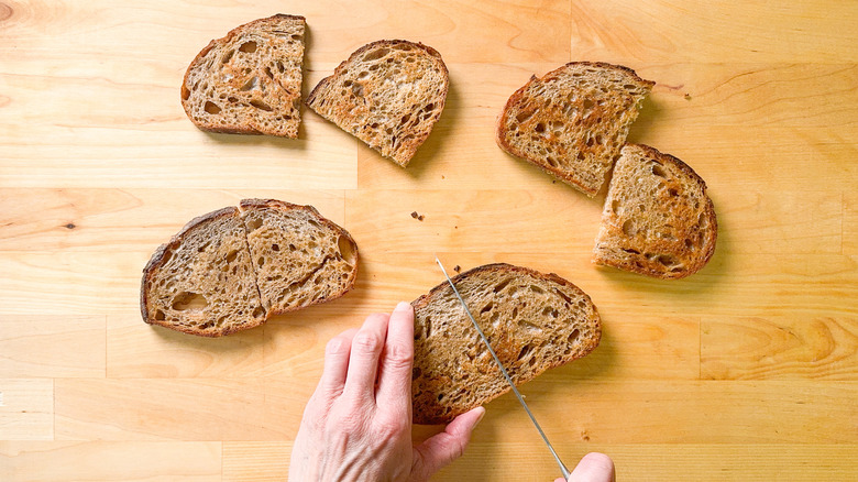 Cutting rye bread slices into halves on cutting board with serrated knife