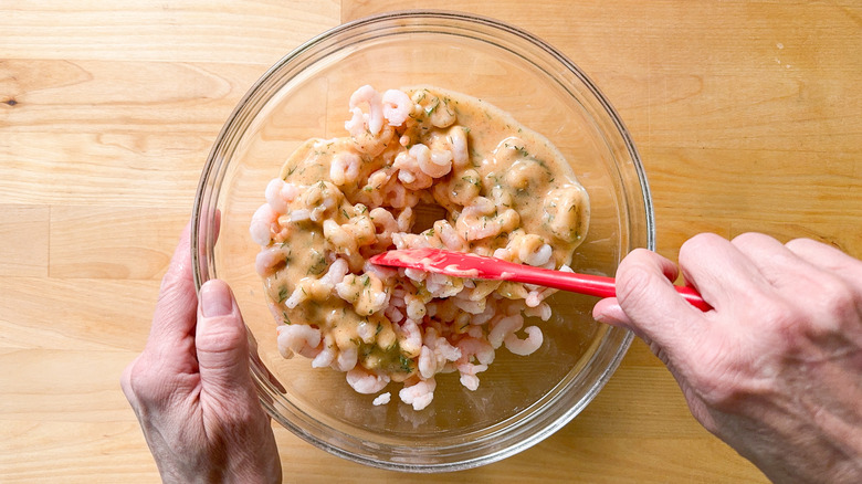 Tossing salad shrimp with mayonnaise dressing in glass bowl with rubber spatula
