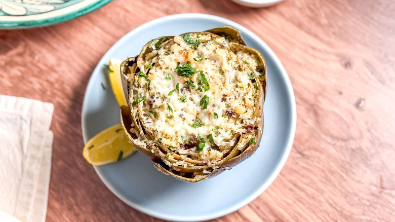 Sicilian-style stuffed artichoke on blue plate with lemon