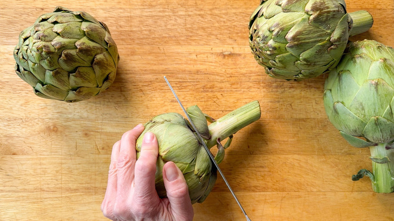 Trimming stems from artichokes on cutting board