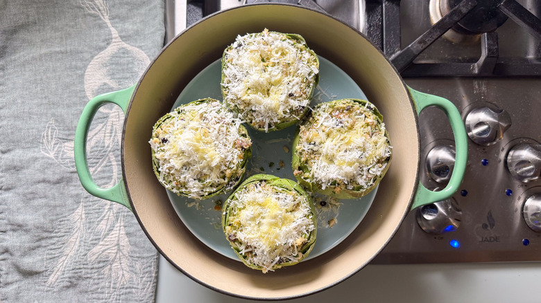 Sicilian-style stuffed artichokes topped with shredded cheese and olive oil in steam bath on stovetop