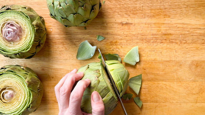 Cutting tops off artichokes on cutting board