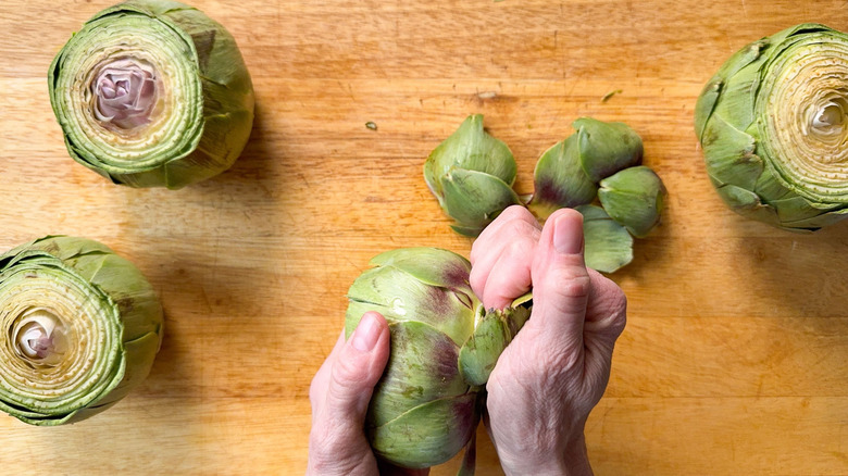 Pulling outer leaves from fresh artichokes on cutting board