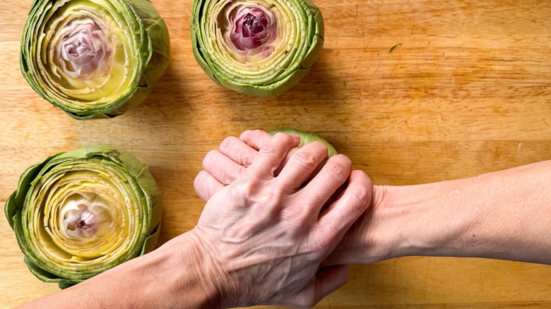 Pressing down on trimmed fresh artichokes to open up the leaves