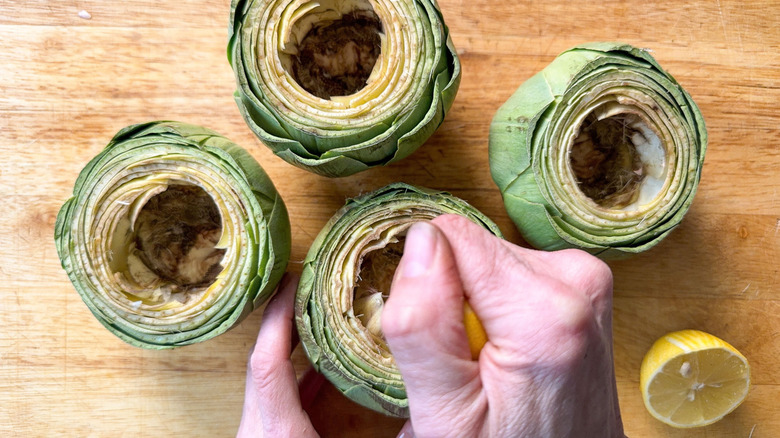 Squeezing fresh lemon over cleaned artichokes on cutting board