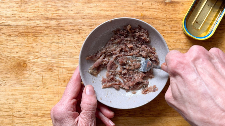 Mashing anchovies into a paste in a bowl with a fork