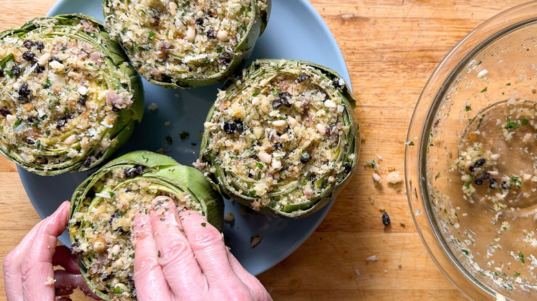 Filling artichokes with stuffing on plate on cutting board