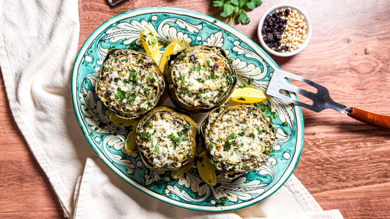 Sicilian-style stuffed artichokes on serving platter with spatula and garnishes