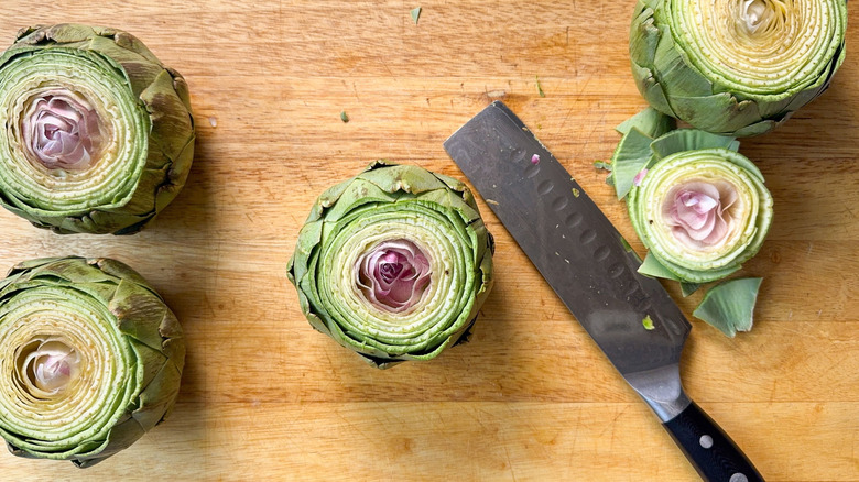 Trimmed fresh artichokes on cutting board with chef's knife