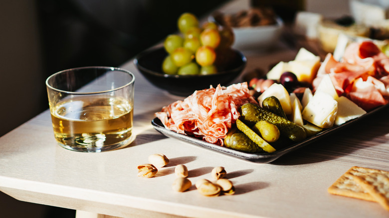 Charcuterie, cheese, fruit, and nuts arranged alongside a drink in a short glass