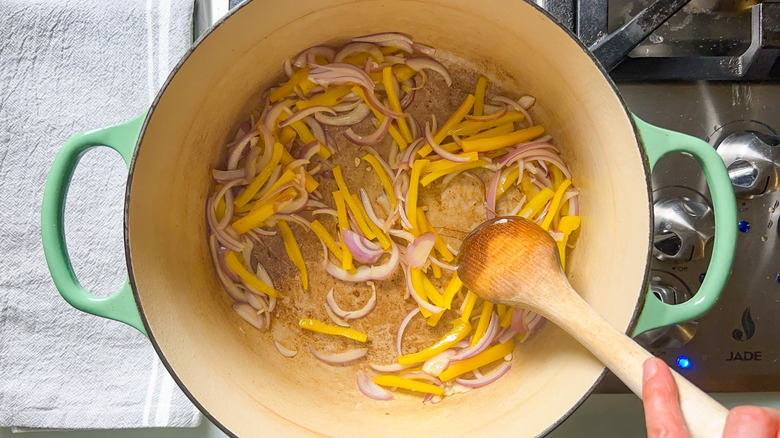 Red onion, yellow bell pepper, and garlic in pot with wooden spoon