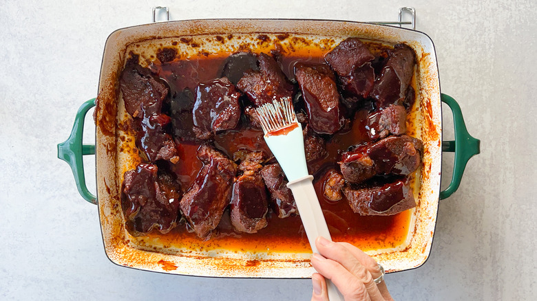 Basting barbecue sauce on baked beef short ribs in pan