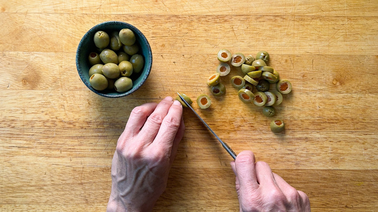 Slicing pimento-stuffed Spanish olives on cutting board