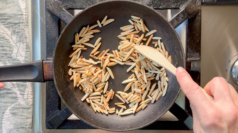 Toasting slivered almonds in skillet on stovetop with wooden spoon