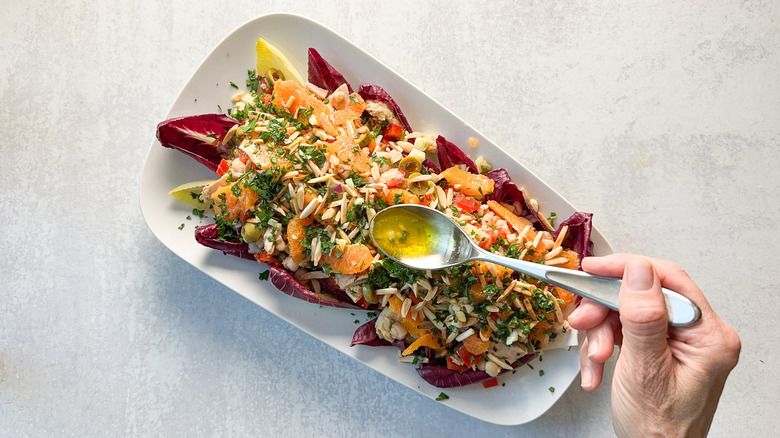 Adding dressing to Spanish-inspired tuna salad with white beans and oranges on platter