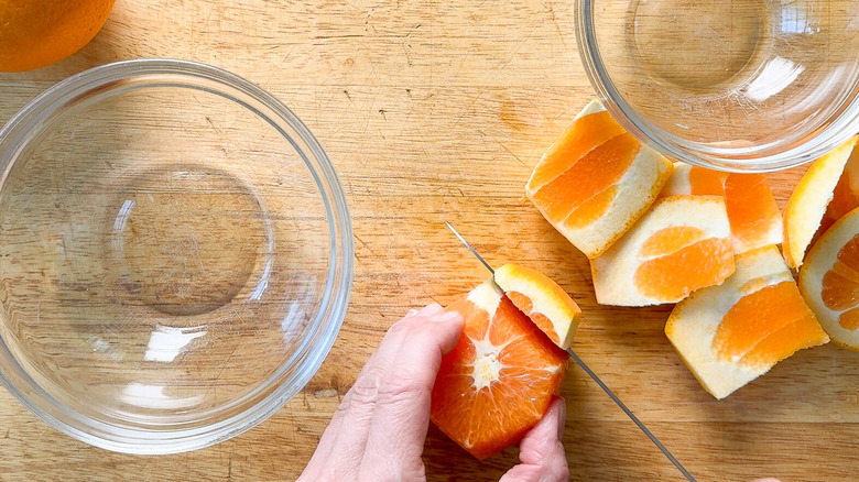 Cutting the peel off an orange on a cutting board with bowls