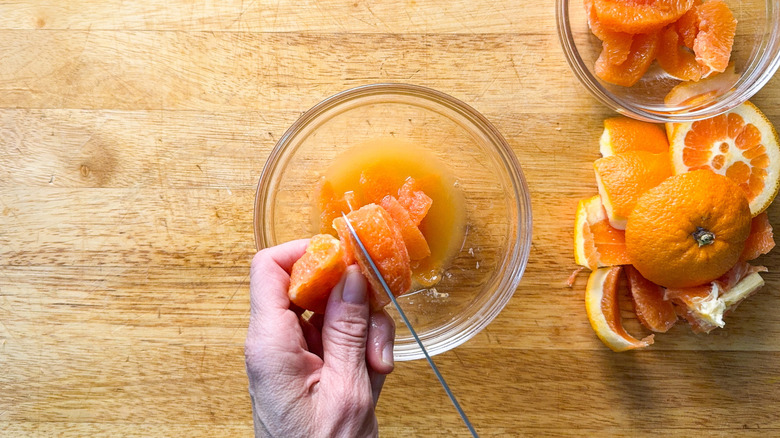 Cutting orange segments away from membranes over bowl on cutting board with orange peels