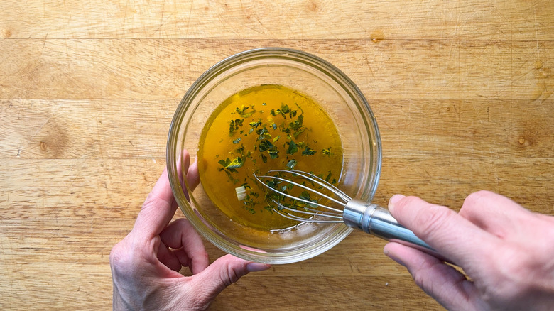 Whisking together olive oil, orange juice, vinegar and fresh oregano in glass bowl on cutting board