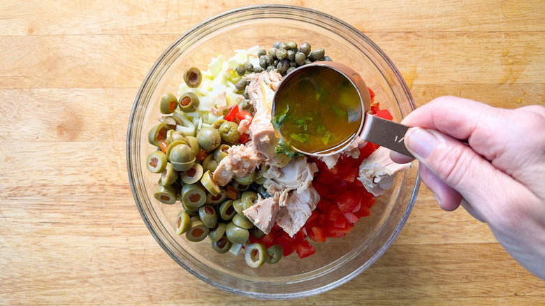 Adding dressing to Spanish-inspired tuna salad in glass bowl