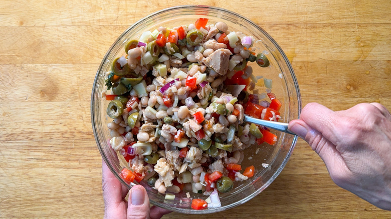 Tossing Spanish-inspired tuna salad with fork in glass bowl