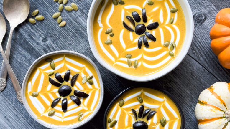 Spooky pumpkin curry Halloween soup in bowls with sour cream spiderwebs and black olive spiders