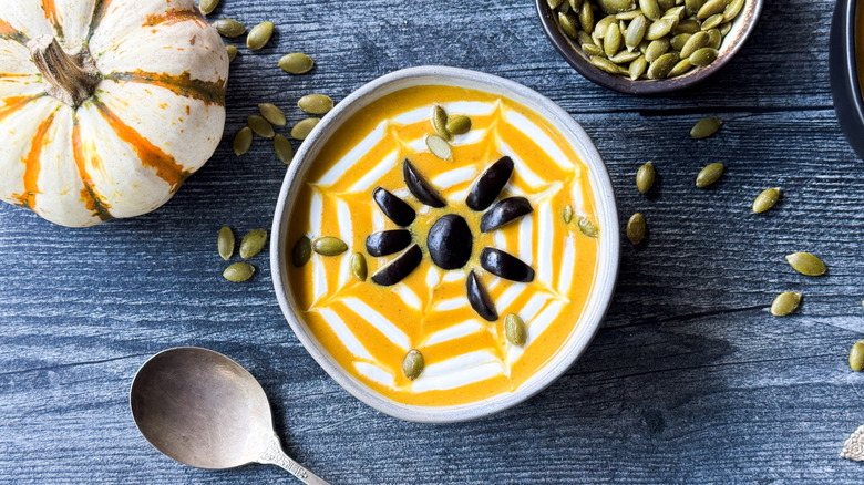 Spooky pumpkin curry Halloween soup in bowl with sour cream spiderweb, black olive spider, and roasted pumpkin seeds