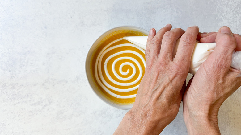 Piping a spiral design of sour cream onto pumpkin curry soup using pastry bag