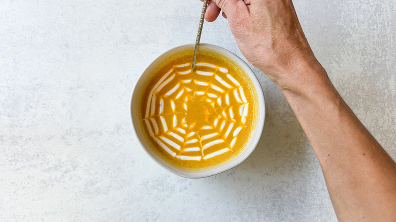 Making a spiderweb design on pumpkin soup with sour cream and a cocktail pick