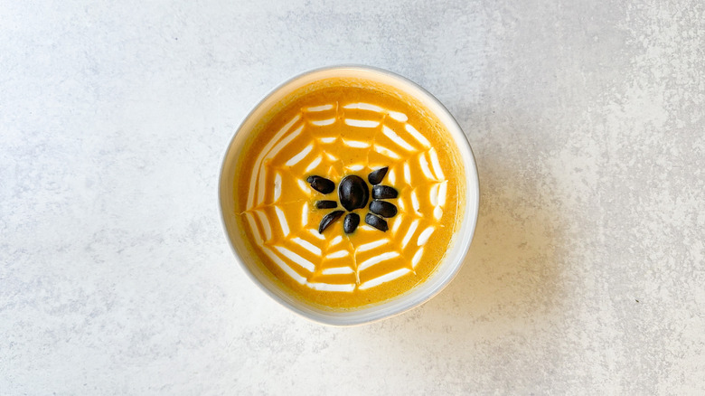 Spooky pumpkin curry Halloween soup with sour cream spiderweb and black olive spider in bowl