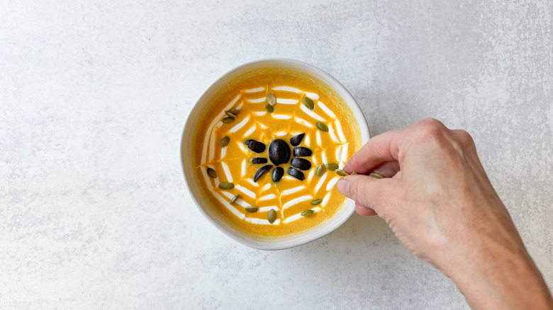 Sprinkling toasted pumpkin seeds on spooky pumpkin curry Halloween soup